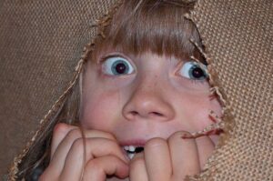 girl looking fearfully from behind a ripped hessian sack